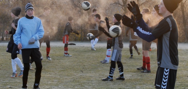 Udendørs foldbold træning en vinterdag, hvor man ser disen og del kolde lys. Spillerne i gang men en øvelse hvor de kaster bolde til hinanden.